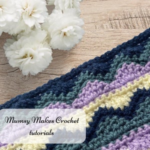 May include: A close-up of a crocheted blanket with stripes of navy blue, green, lavender, and cream yarn. The text "Mumsy Makes Crochet tutorials" is visible in the bottom left corner of the image.