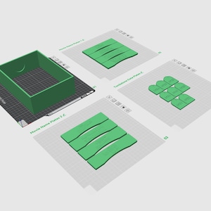 May include: A green display box and several green plates with text, labeled "Movie Name Plates" and "Tombstone Date Plates." The items are arranged on a gray grid background. The display box has a crescent moon cutout.