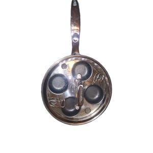 May include: A silver-toned, four-cup egg poacher pan with a long handle. The pan features four individual circular cups for poaching eggs, and a handle for easy use. The pan is designed for stovetop cooking.