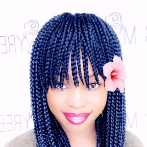 May include: A woman with long blue braids and a pink flower in her hair. She is smiling and looking at the camera.