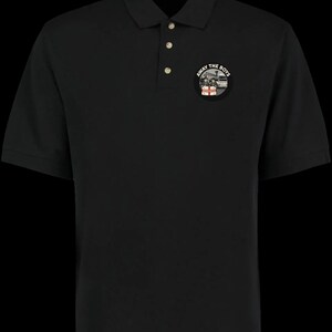 Pode incluir: Camisa polo preta com carcela de tr&ecirc;s bot&otilde;es e mangas curtas. Um patch circular no peito apresenta o texto "AWAY THE BOYS" em torno de uma ilustra&ccedil;&atilde;o de um ve&iacute;culo e pessoas.