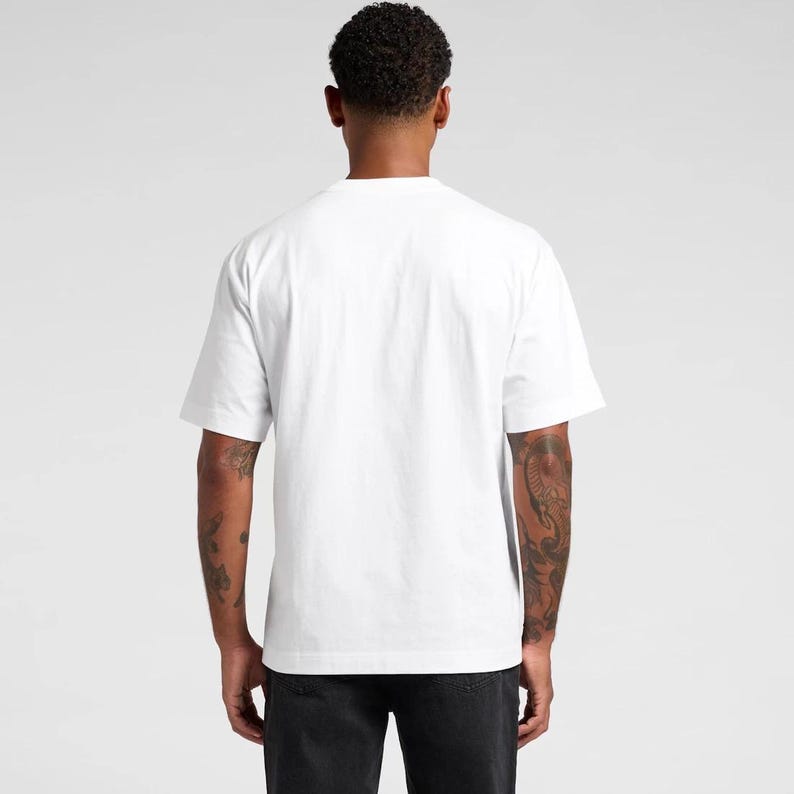 K&ouml;nnte beinhalten: Ein wei&szlig;es T-Shirt mit kurzen &Auml;rmeln. Die R&uuml;ckansicht zeigt das schlichte Design und die Passform des Shirts. Der Stoff ist weich und blickdicht. Das Model tr&auml;gt eine schwarze Hose. Der Hintergrund ist hellgrau.