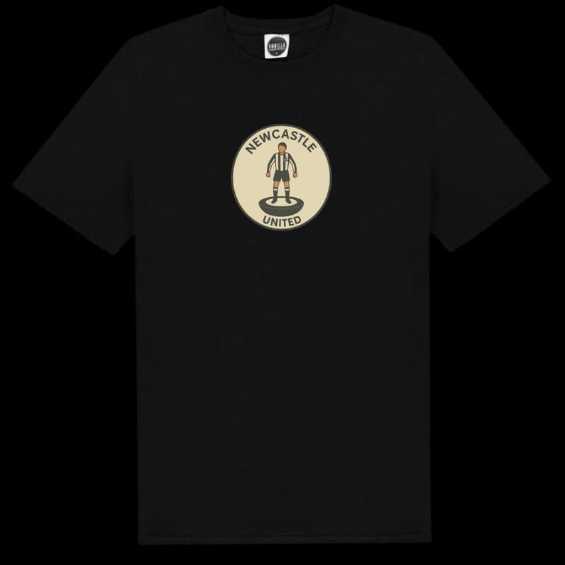 Peut inclure: T-shirt noir avec un &eacute;cusson circulaire repr&eacute;sentant un joueur de football en noir et blanc. L'&eacute;cusson cr&egrave;me porte l'inscription "NEWCASTLE UNITED" en cercle autour du joueur.