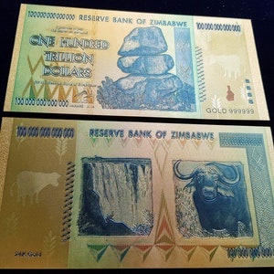 Könnte beinhalten: Ein goldfarbener Banknote aus Simbabwe mit einem Wert von hundert Billionen Dollar. Die Vorderseite des Scheins zeigt einen Steinhaufen und die Rückseite einen Wasserfall und einen Büffel. Der Schein trägt den Schriftzug "Reserve Bank of Zimbabwe".