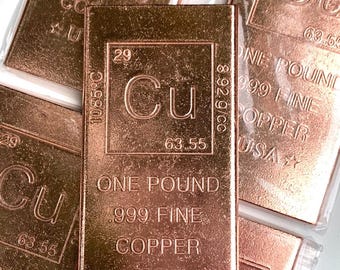 May include: A rectangular copper bar featuring the periodic table symbol Cu, atomic number 29, and atomic weight 63.55. The bar is stamped with One Pound, .999 Fine Copper, USA, and 1085 degrees Celsius melting point.