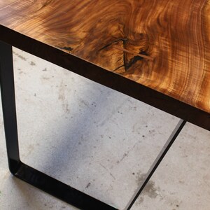 May include: A wooden table top with a live edge and natural wood grain. The table top is supported by a black metal frame.