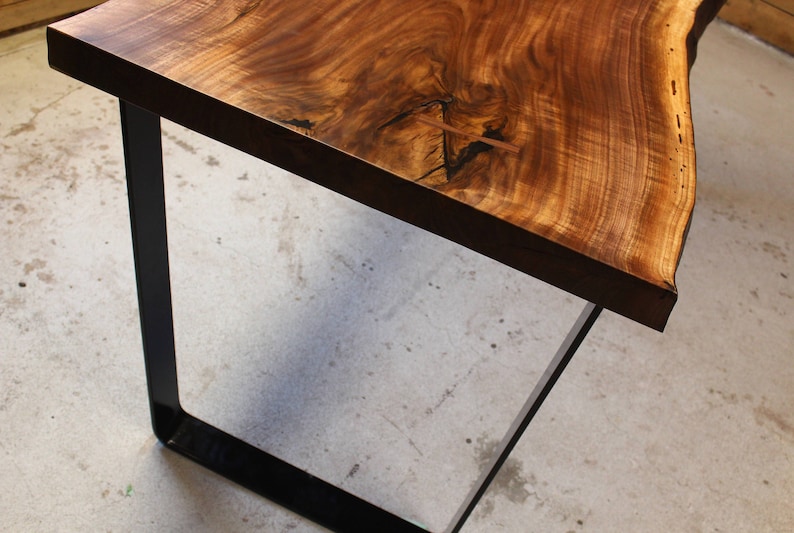 May include: A wooden table top with a live edge and natural wood grain. The table top is supported by a black metal frame.