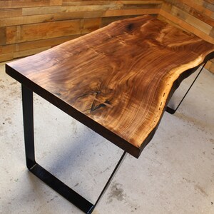 May include: A live edge walnut wood table with a natural wood finish and black metal legs. The table has a unique, organic shape and is perfect for a modern or rustic decor.