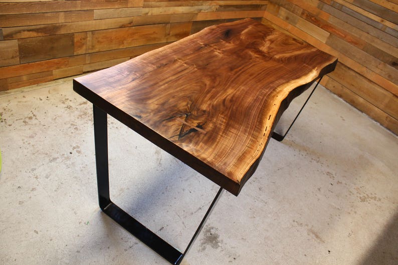 May include: A live edge walnut wood table with a natural wood finish and black metal legs. The table has a unique, organic shape and is perfect for a modern or rustic decor.