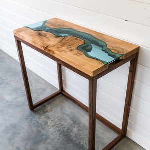 Puede incluir: Una mesa consola de madera con un diseño de río de vidrio transparente en la parte superior. La mesa tiene un marco de madera marrón oscuro.
