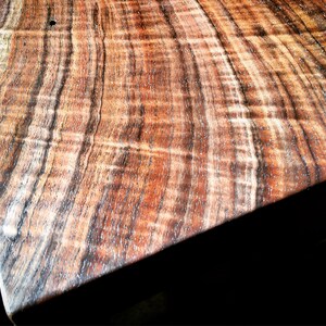 May include: Close-up of a wooden table top with a rich brown and black wood grain pattern. The wood has a natural, polished finish.