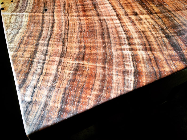 May include: Close-up of a wooden table top with a rich brown and black wood grain pattern. The wood has a natural, polished finish.
