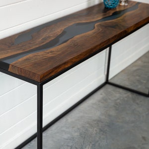 May include: A dark wood console table with a black metal frame. The table top has a black epoxy river design.