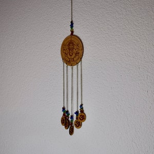 May include: A wooden wind chime with a circular design featuring a deity and the symbol Om. The chime has multiple strands of beads in shades of blue, green, and red.