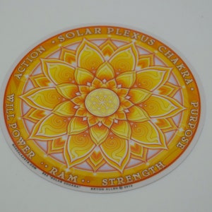 Puede incluir: Una pegatina circular amarilla y naranja con un diseño de mandala. El texto "Solar Plexus Chakra" está escrito alrededor del exterior del círculo. Las palabras "Action", "Will Power", "Ram", "Strength", "Purpose" también están escritas alrededor del círculo.