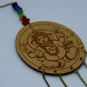 May include: A wooden wall hanging with a carved image of the Hindu deity Ganesha. The hanging has a chain with colorful beads and four chains hanging from the bottom.