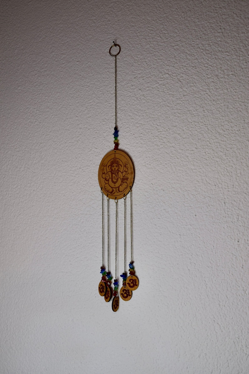 May include: A wooden wind chime with a circular design featuring a deity and the symbol Om. The chime has multiple strands of beads in shades of blue, green, and red.