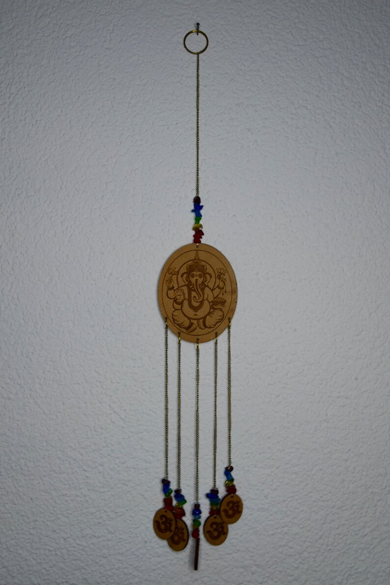 May include: A wooden wind chime with a circular design featuring an image of the Hindu deity Ganesha. The chime has five strands of beads and five charms with the Om symbol.