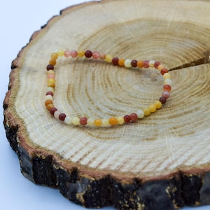 Op de afbeelding: Een veelkleurige kralen armband met rode, oranje en gele kralen op een houten achtergrond.