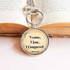 May include: A silver keychain with a round charm featuring a quote by Julius Caesar: "I came, I saw, I conquered". The charm has a vintage parchment background.