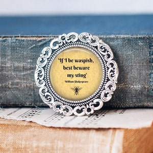 Op de afbeelding: Een rond, zilverkleurig, versierd frame met een citaat erin: "If I be waspish, best beware my sting." Het citaat wordt toegeschreven aan William Shakespeare. Onder het citaat staat een kleine bij-illustratie.