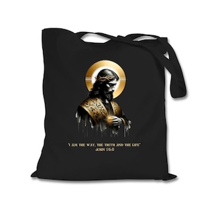 Puede incluir: Bolsa de tela negra con una ilustración dorada y blanca de Jesucristo con una corona de espinas y un halo. El texto 'I AM THE WAY, THE TRUTH AND THE LIFE' y 'JOHN 14:8' está impreso debajo de la imagen.