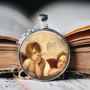 May include: A silver pendant necklace with a round glass cameo featuring a painting of two cherubs. The cherubs are depicted with wings and are looking at each other. The cameo is set in a silver frame.