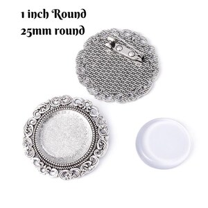 May include: Silver-toned round brooch components with decorative edges. The image includes a brooch back with a pin, a bezel, and a clear glass cabochon. Text reads "1 inch Round" and "25mm round".