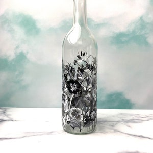 K&ouml;nnte beinhalten: Eine klare Glasflasche mit einem schwarz-wei&szlig;en Blumenmuster, das auf die Oberfl&auml;che gemalt ist. Die Flasche ist leer und hat einen langen Hals.