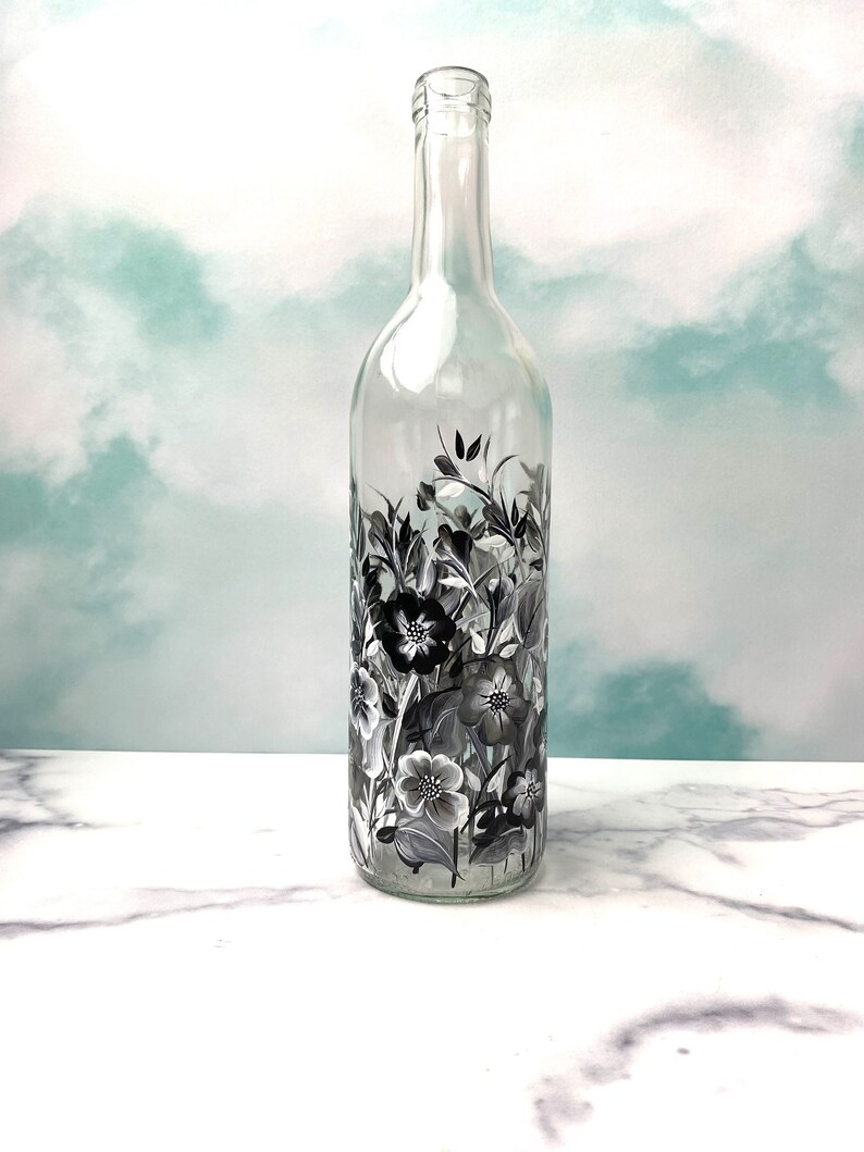 K&ouml;nnte beinhalten: Eine klare Glasflasche mit einem schwarz-wei&szlig;en Blumenmuster, das auf die Oberfl&auml;che gemalt ist. Die Flasche ist leer und hat einen langen Hals.