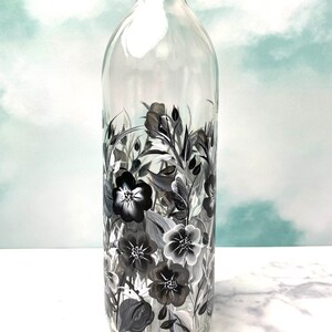 K&ouml;nnte beinhalten: Eine klare Glasflasche mit einem schwarz-wei&szlig;en Blumenmuster, das auf die Seite gemalt ist. Die Blumen sind stilisiert und haben einen Vintage-Look.