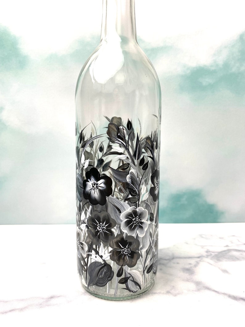 K&ouml;nnte beinhalten: Eine klare Glasflasche mit einem schwarz-wei&szlig;en Blumenmuster, das auf die Seite gemalt ist. Die Blumen sind stilisiert und haben einen Vintage-Look.