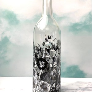 K&ouml;nnte beinhalten: Eine klare Glas-Weinflasche mit schwarzen und wei&szlig;en Blumenmustern, die auf die Oberfl&auml;che gemalt sind.