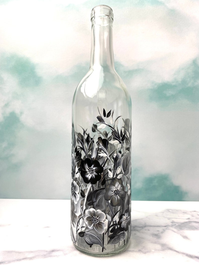 K&ouml;nnte beinhalten: Eine klare Glas-Weinflasche mit schwarzen und wei&szlig;en Blumenmustern, die auf die Oberfl&auml;che gemalt sind.