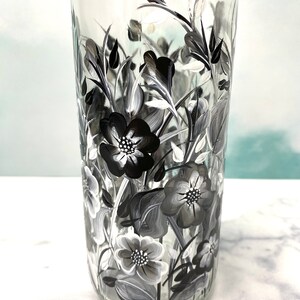 K&ouml;nnte beinhalten: Eine klare Glasflasche mit einem schwarz-wei&szlig;en Blumenmuster, das auf die Seite gemalt ist. Die Blumen sind stilisiert und haben einen Vintage-Look.