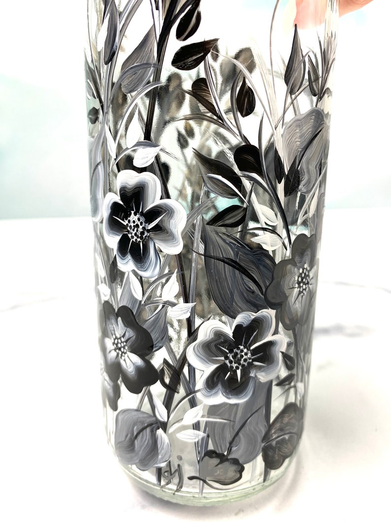 K&ouml;nnte beinhalten: Eine klare Glasvase mit einem schwarz-wei&szlig;en Blumenmuster, das auf die Seite gemalt ist. Die Blumen sind stilisiert und haben einen einfachen, eleganten Look.