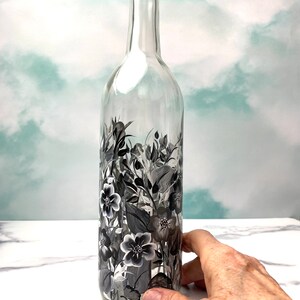 K&ouml;nnte beinhalten: Eine klare Glasflasche mit einem schwarz-wei&szlig;en Blumenmuster, das auf die Seite gemalt ist. Die Flasche ist leer und hat eine strukturierte Oberfl&auml;che.