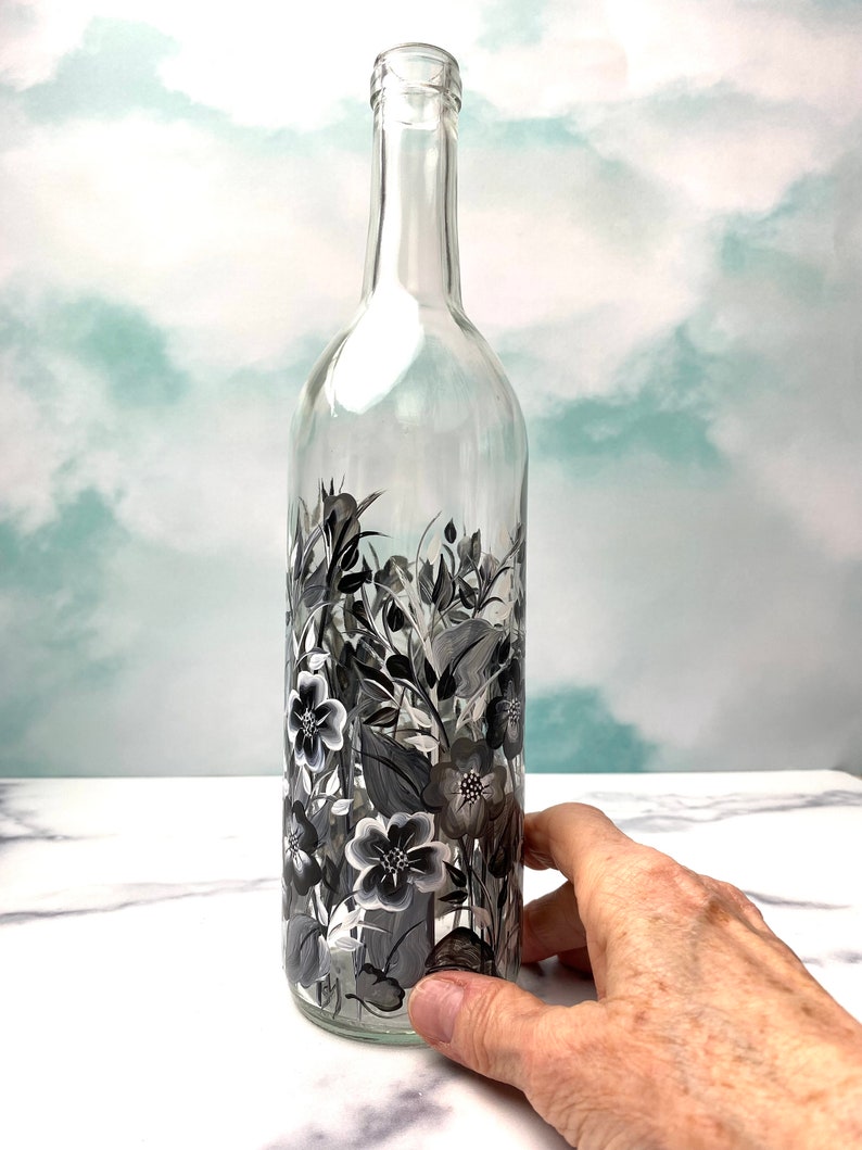 K&ouml;nnte beinhalten: Eine klare Glasflasche mit einem schwarz-wei&szlig;en Blumenmuster, das auf die Seite gemalt ist. Die Flasche ist leer und hat eine strukturierte Oberfl&auml;che.