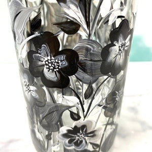 K&ouml;nnte beinhalten: Eine klare Glasvase mit einem schwarzen und wei&szlig;en Blumendesign. Die Vase ist handbemalt mit stilisierten Blumen und Bl&auml;ttern.