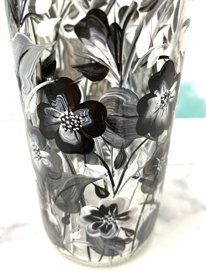 K&ouml;nnte beinhalten: Eine klare Glasvase mit einem schwarzen und wei&szlig;en Blumendesign. Die Vase ist handbemalt mit stilisierten Blumen und Bl&auml;ttern.