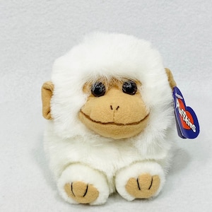 May include: White plush monkey toy with brown eyes and a brown nose. The monkey is sitting with its legs crossed and has a small heart-shaped tag that says "Puffkins" on it.
