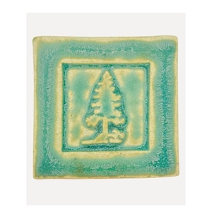 May include: A square ceramic tile featuring a raised relief of a pine tree in the center. The tile has a glossy glaze with a color gradient transitioning from a deep turquoise border to a lighter, creamy yellow center around the tree motif.