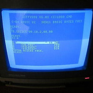 Könnte beinhalten: Ein alter Computermonitor, der blauen Text auf blauem Hintergrund anzeigt. Der Text enthält "JIFFYDDS V6.01 (C)1989 CMD" und "C-64 BASIC V2 38911 BASIC BYTES FREE". Der Bildschirm zeigt Dateinamen und Verzeichnislisten.