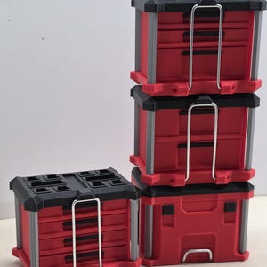 May include: A set of modular storage units in red, black, and gray. One unit is a single-drawer box, while the other is a stack of three drawers. Each unit features a black top with recessed sections, gray vertical corner supports, and a metal latch.