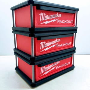 May include: Three red and black storage containers stacked on top of each other. Each container has the words "Miniwaukee PACKOUT" in white lettering. The containers are rectangular with black frames and silver accents.