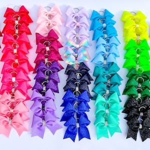 May include: A collection of 20 different colour glitter keychains with a rhinestone accent. Each keychain has 5 bows.