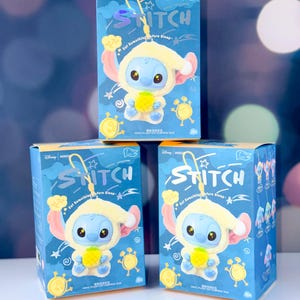 May include: Three blue boxes featuring a Stitch character in a yellow outfit holding a pineapple. The boxes have the word "STITCH" in a stylized font and the phrase "Eat Something before Sleep". The boxes are on a white surface.