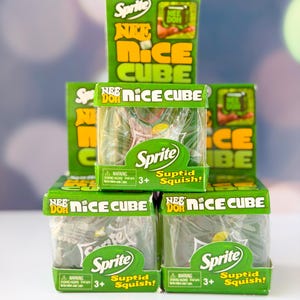 Pode incluir: Uma pilha de cinco caixas verdes e amarelas Nee Doh Nice Cube com a marca Sprite. Cada caixa quadrada tem uma janela de plástico transparente que mostra o cubo macio no interior, com o texto Nee Doh, Nice Cube, Sprite e Suptid Squish.