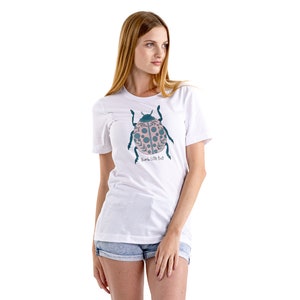 May include: White t-shirt with a pink and teal ladybug graphic and the text "Humble Little Bug".