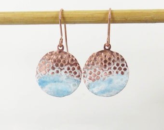 May include: A pair of copper and white enamel earrings with a hammered texture. The earrings are round and have a light blue enamel design.